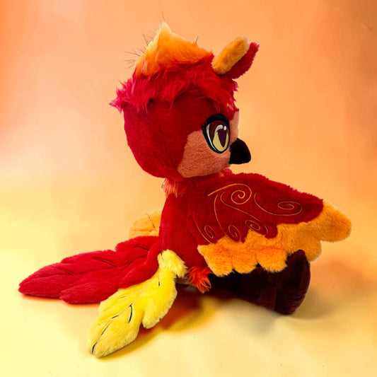 Side seated view of Cinder the Phoenix, a red, orange, gold phoenix plush.