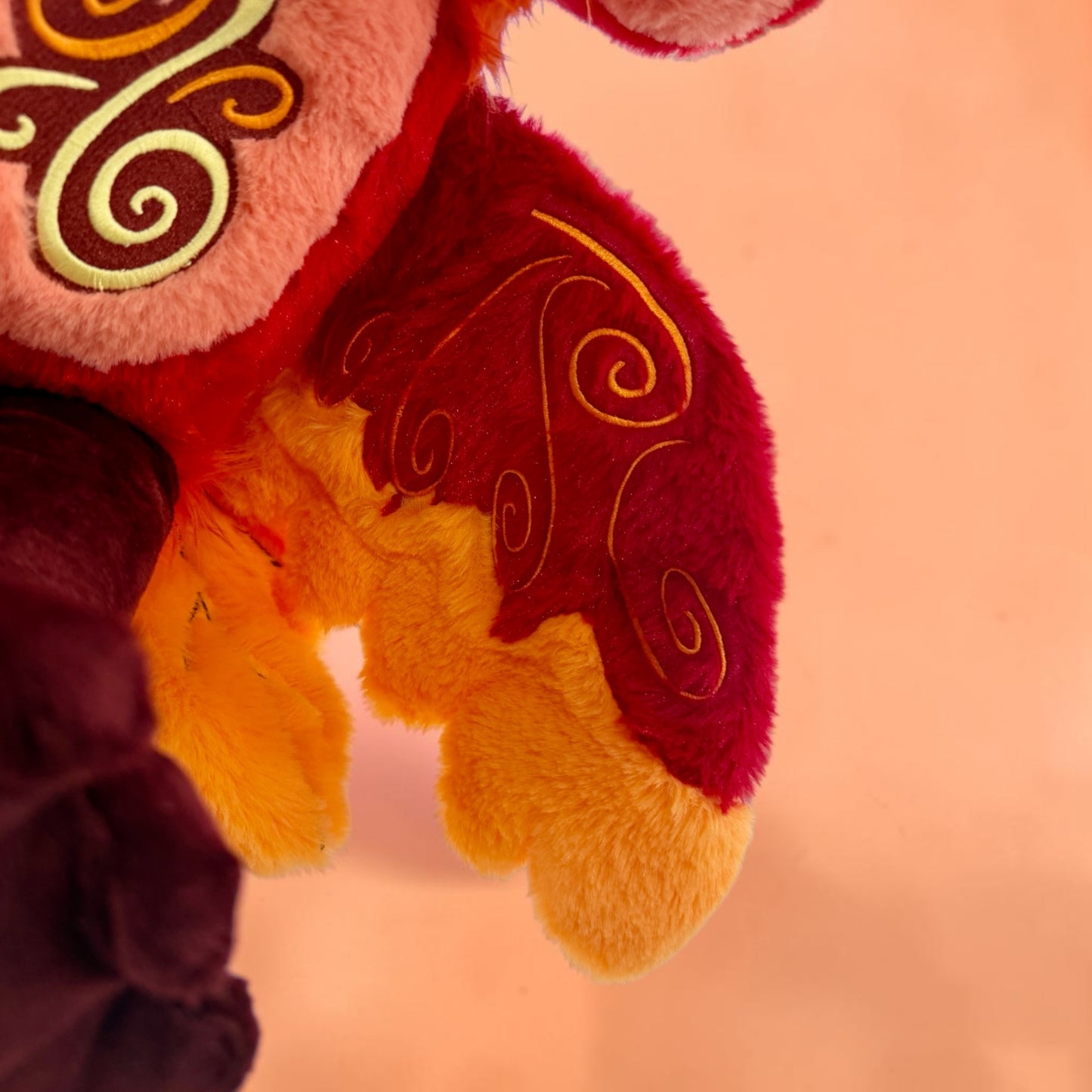 Wing detail of Cinder the Phoenix, a red, orange, gold phoenix plush.
