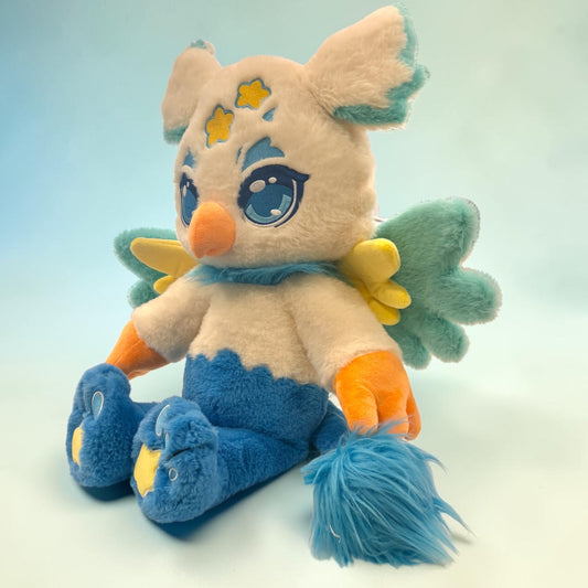 Three-quarter seated view of Luca the Griffin, a cream, blue, gold griffin plush.