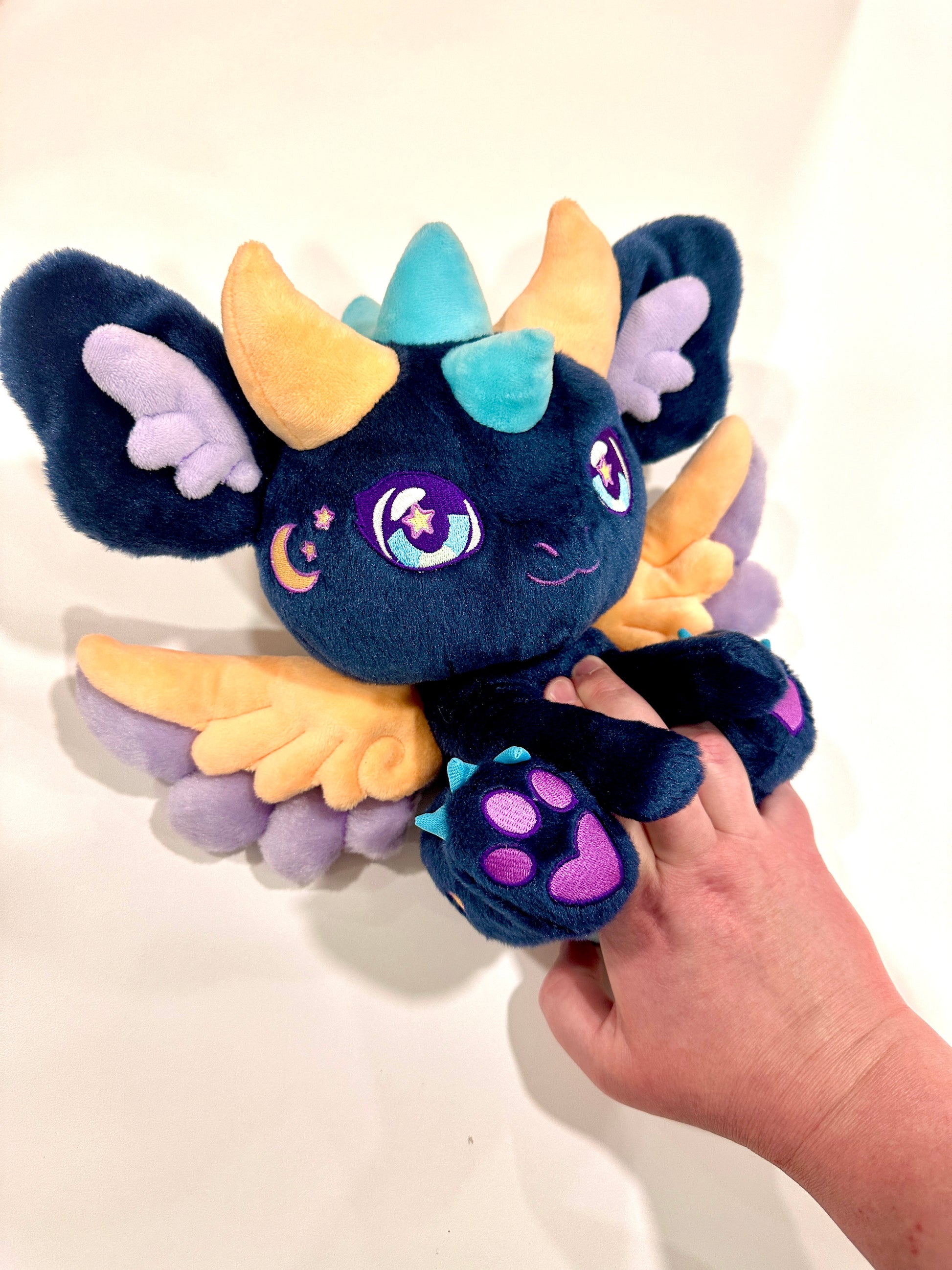 Handheld scale view of Calypso, a navy, peach, turquoise dragon plush.