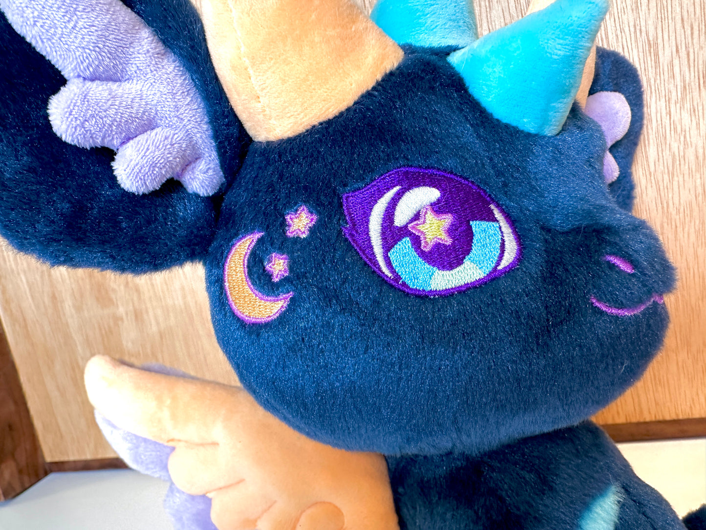 Face detail of Calypso, a navy, peach, turquoise dragon plush.