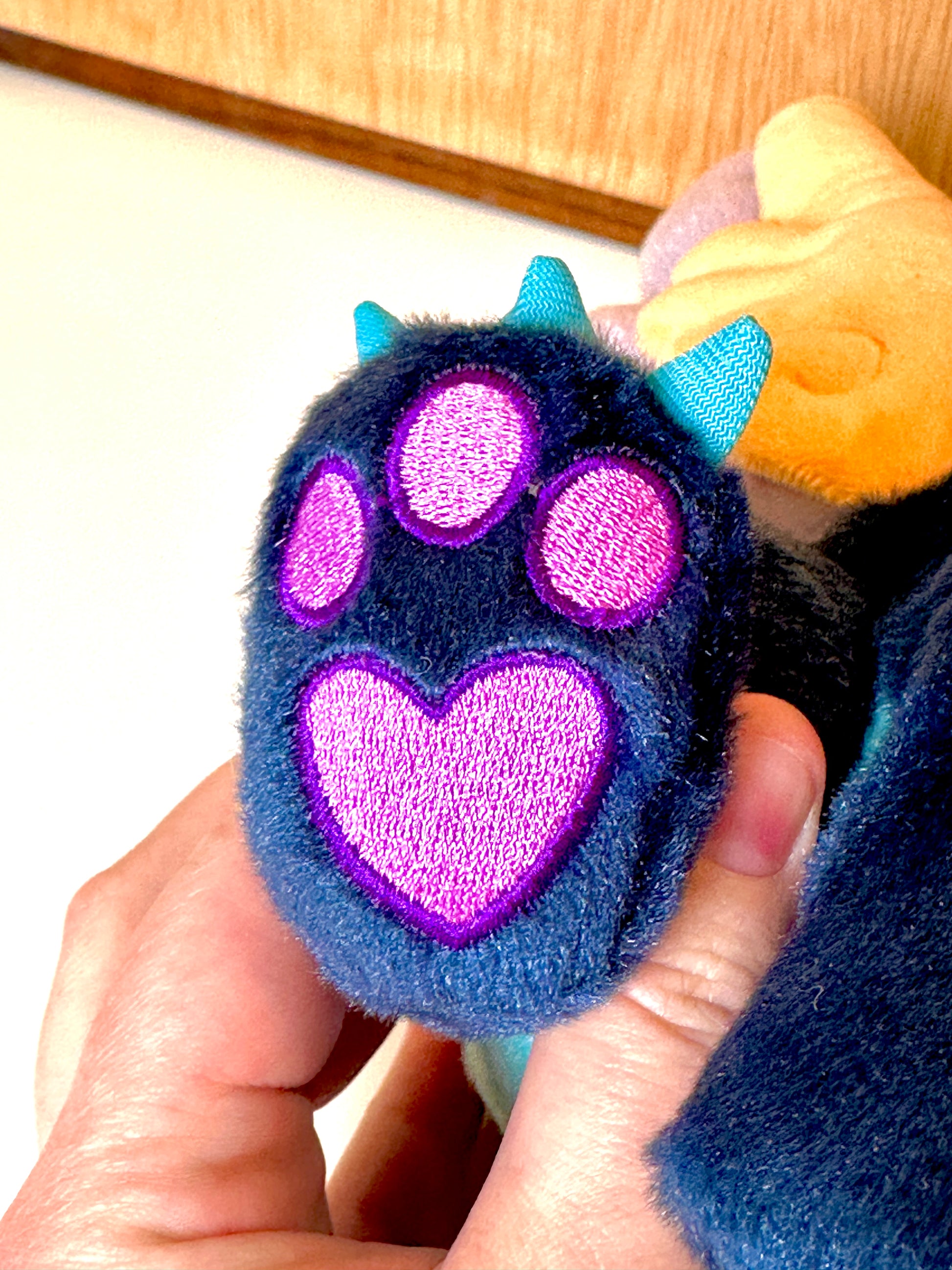 Paw embroidery detail of Calypso, a navy, peach, turquoise dragon plush.