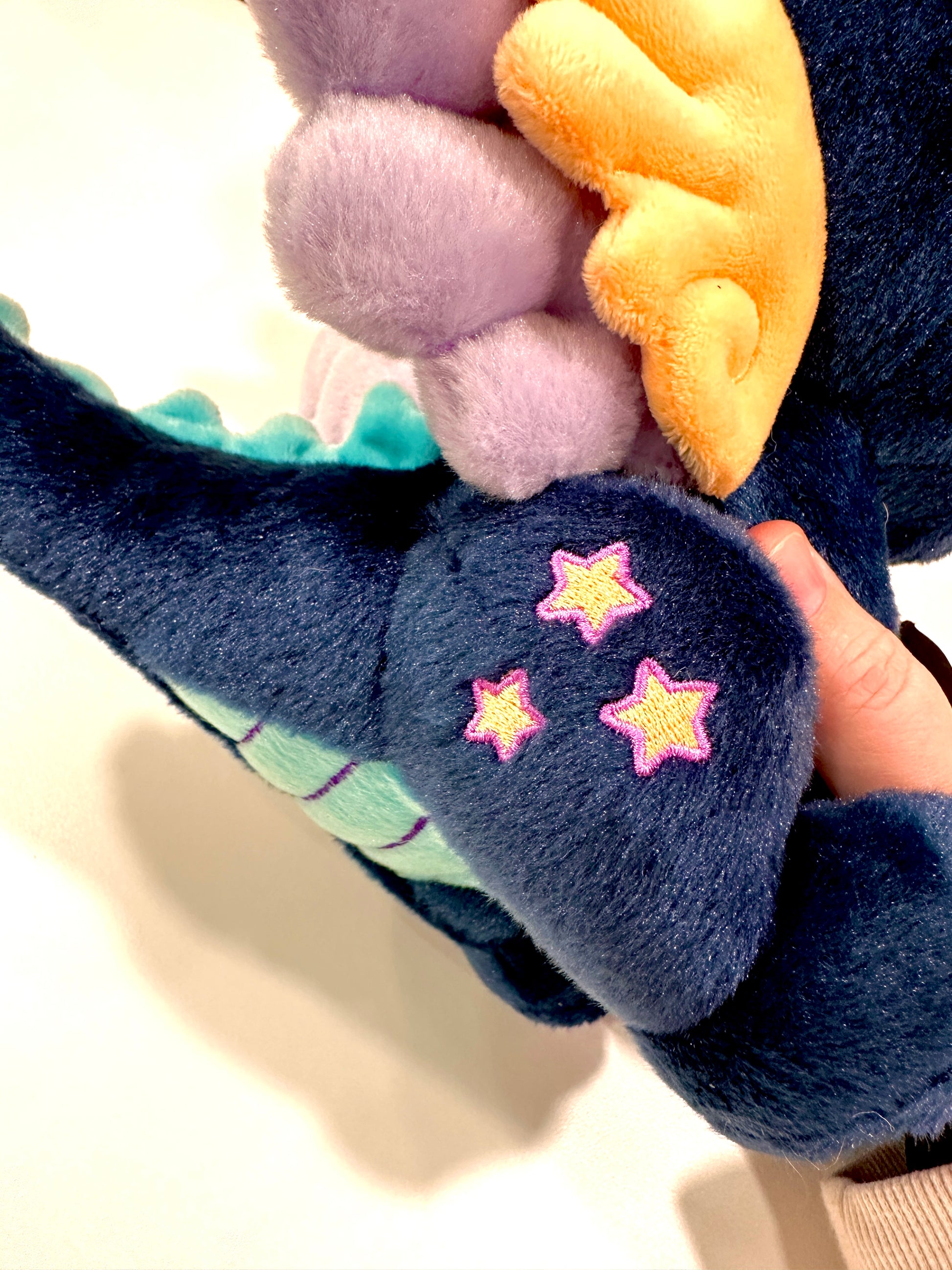 Tail detail of Calypso, a navy, peach, turquoise dragon plush.