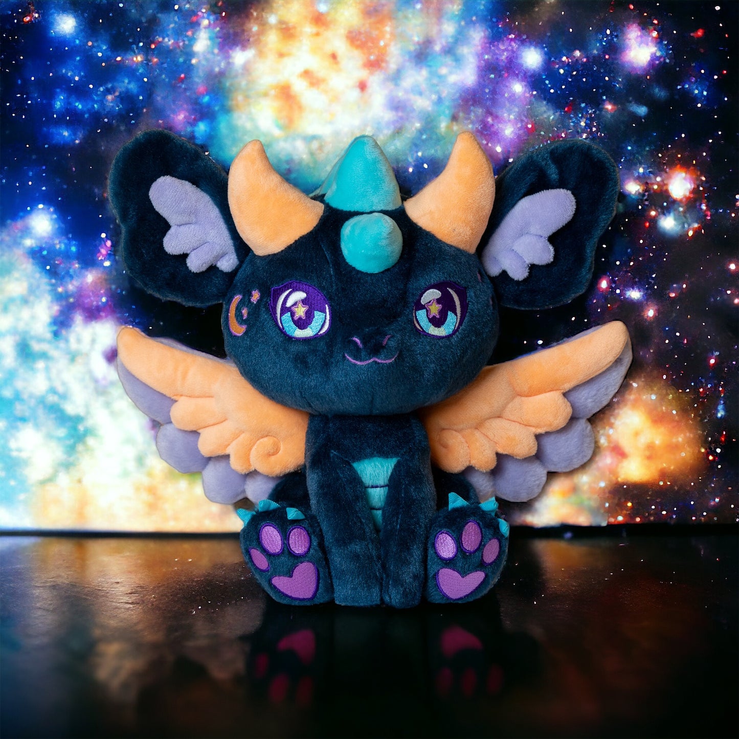 Space lifestyle image of Calypso, a navy, peach, turquoise dragon plush.