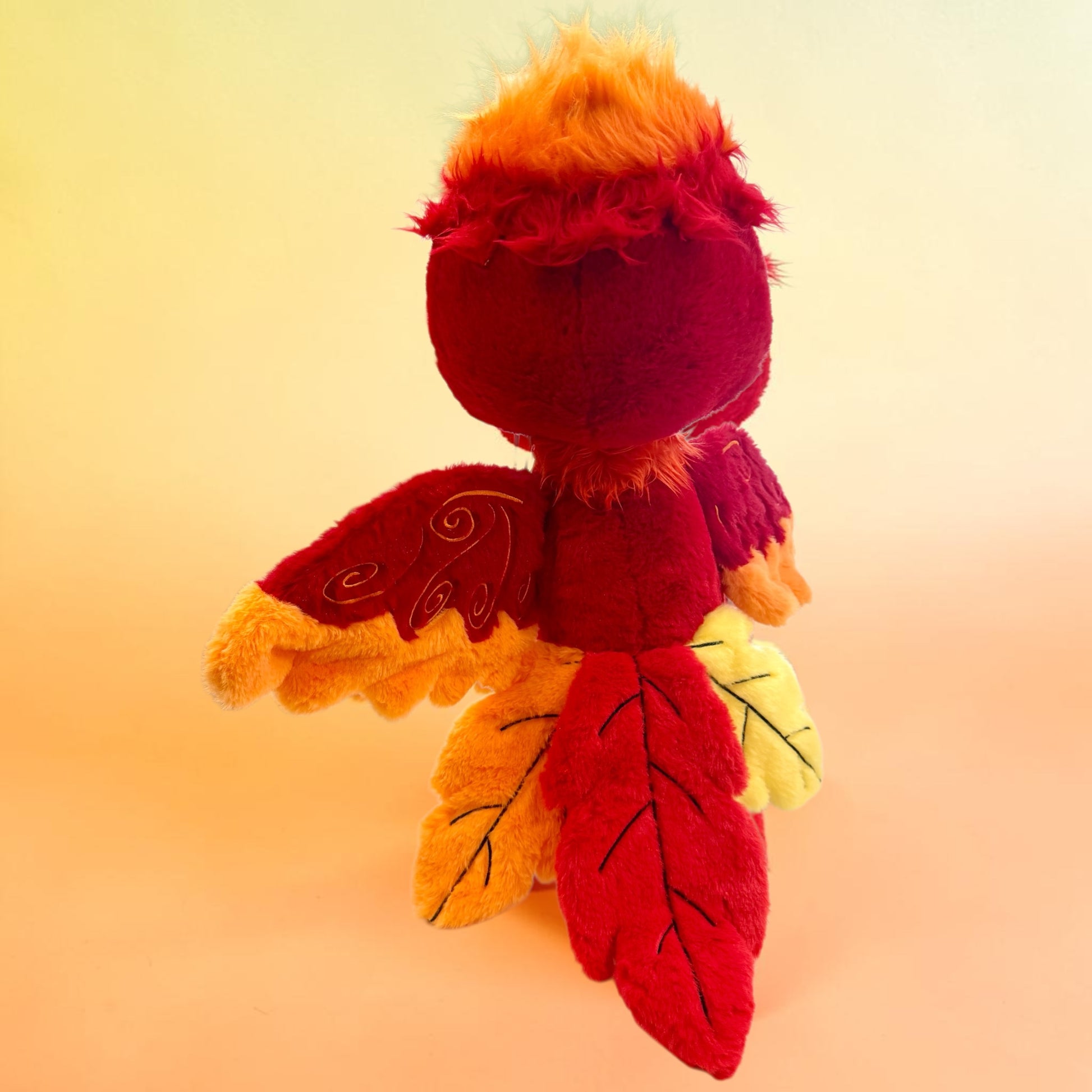 Back view of Cinder the Phoenix, a red, orange, gold phoenix plush.