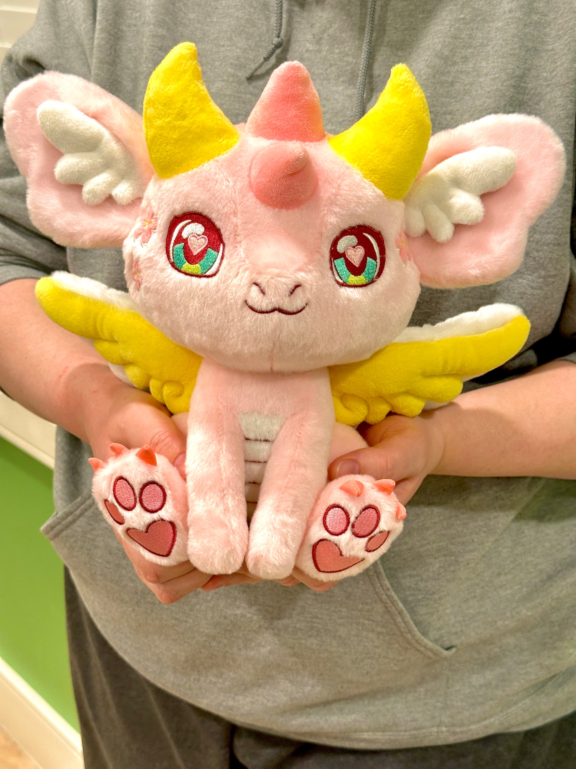 Handheld scale view of Ella, a pink, yellow, white dragon plush.