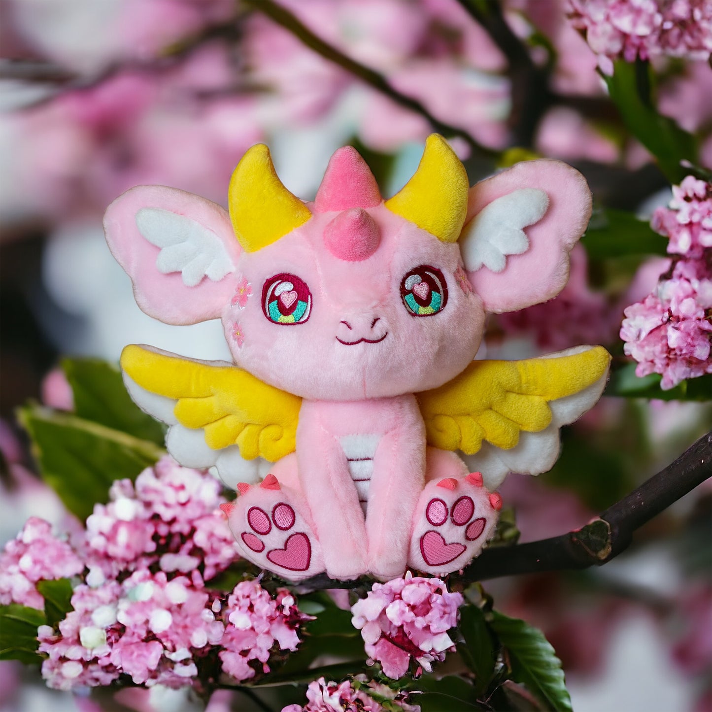 Alternate cherry blossom lifestyle image of Ella, a pink, yellow, white dragon plush.