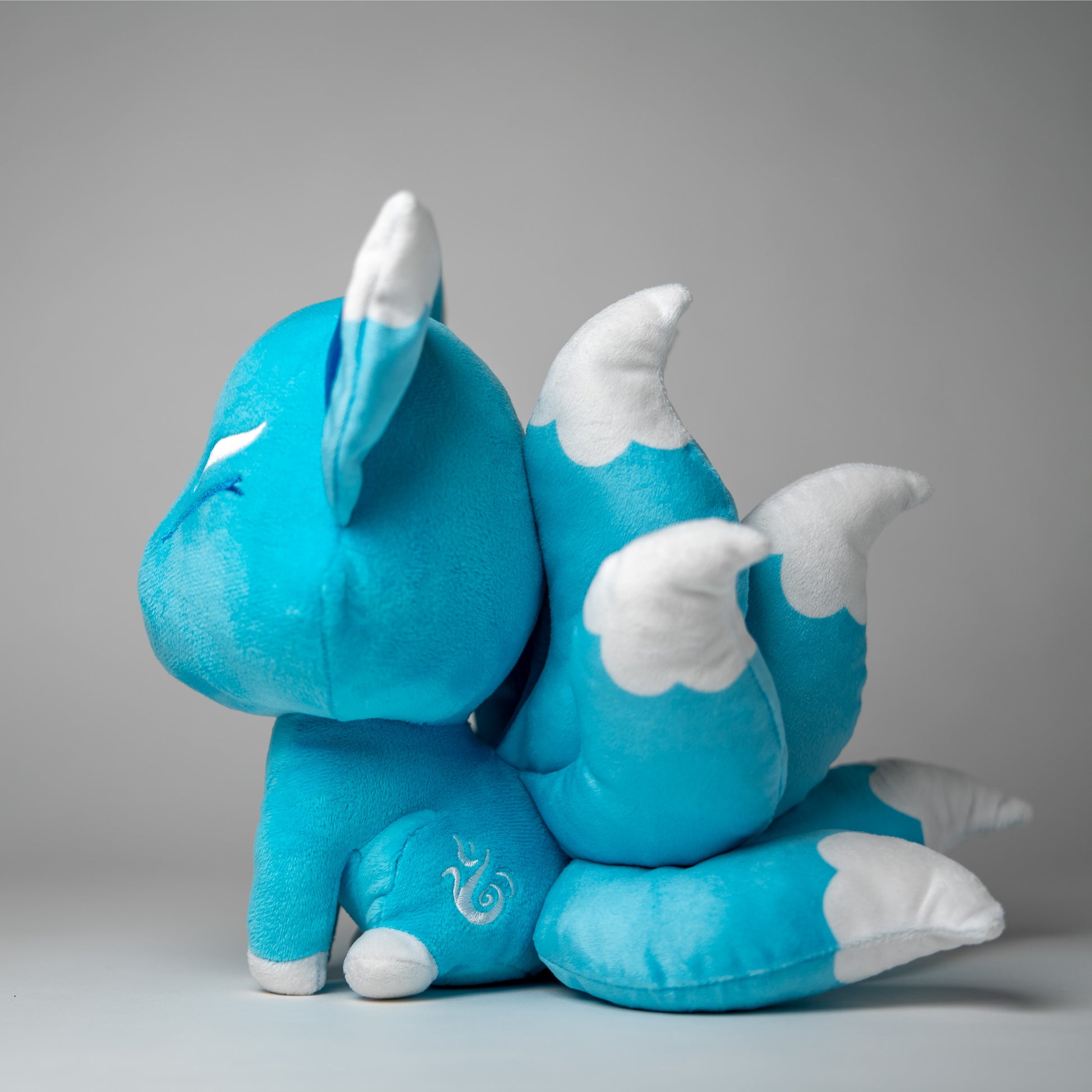 Three-quarter view of Ellies, a turquoise, white, silver kitsune plush.