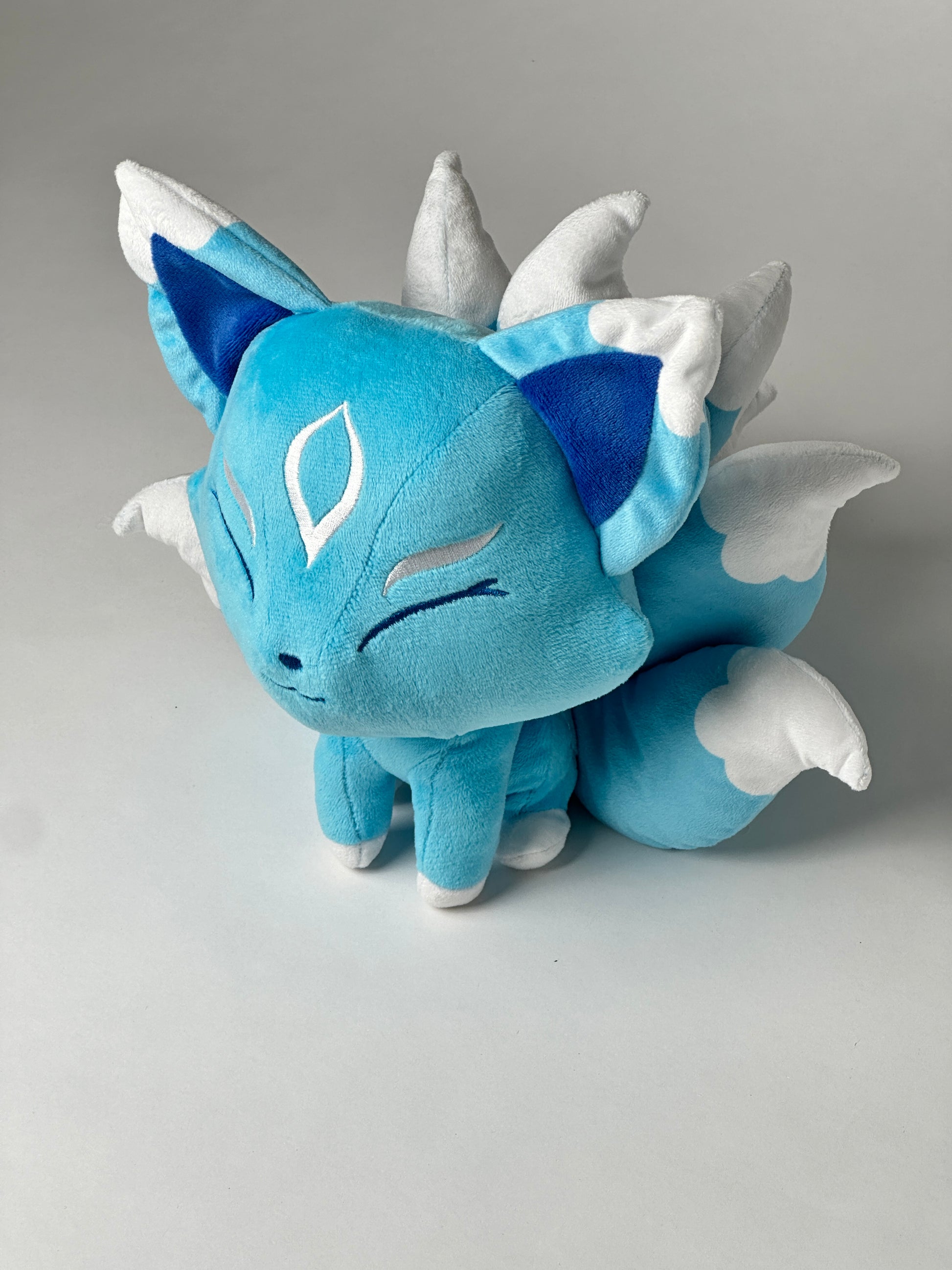 Top view of Ellies, a turquoise, white, silver kitsune plush.