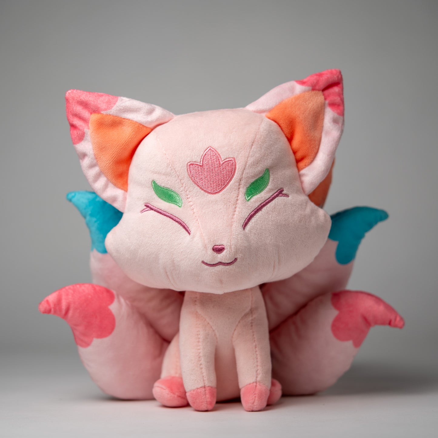 Front view of Flora, a pink, white, turquoise kitsune plush.