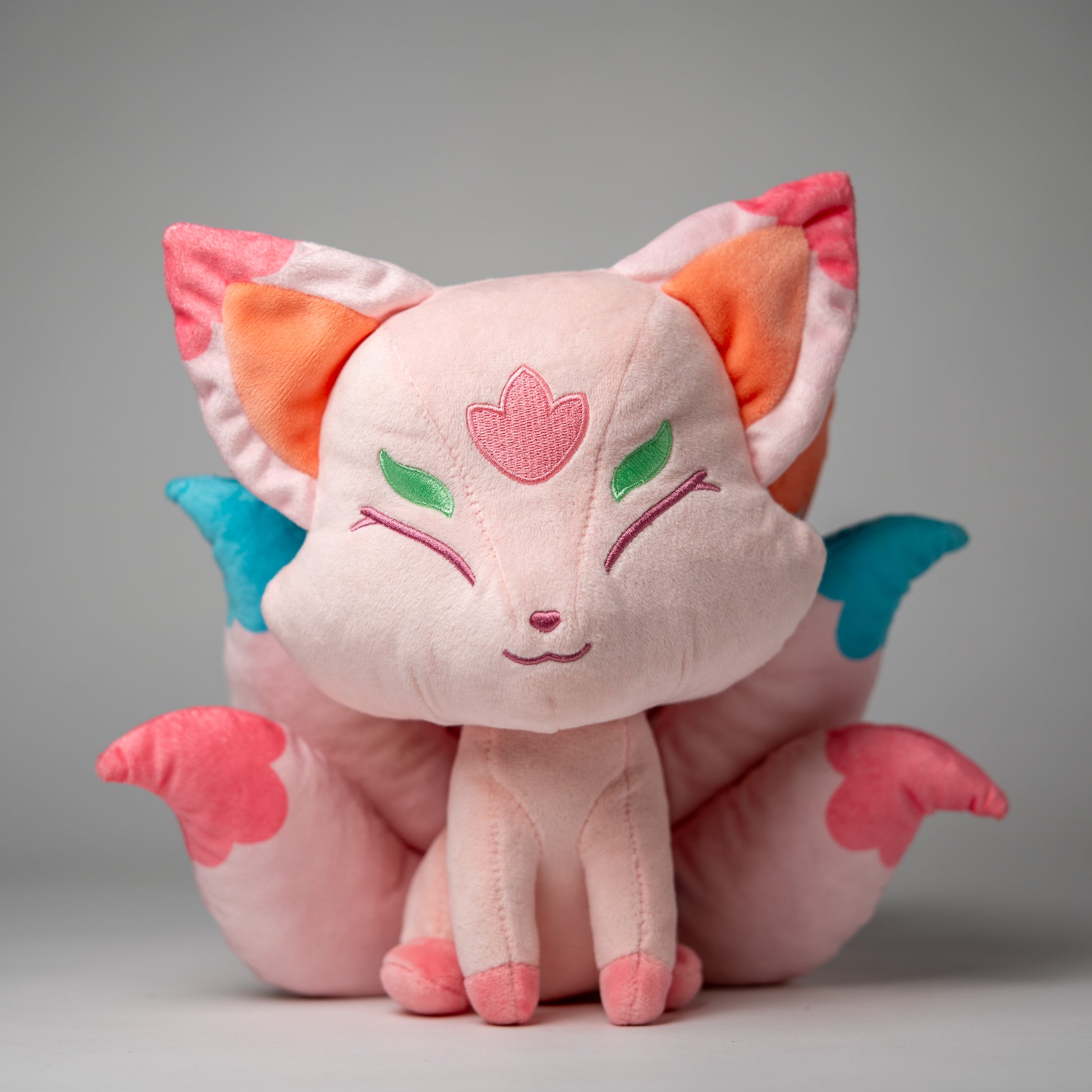 Front view of Flora, a pink, white, turquoise kitsune plush.