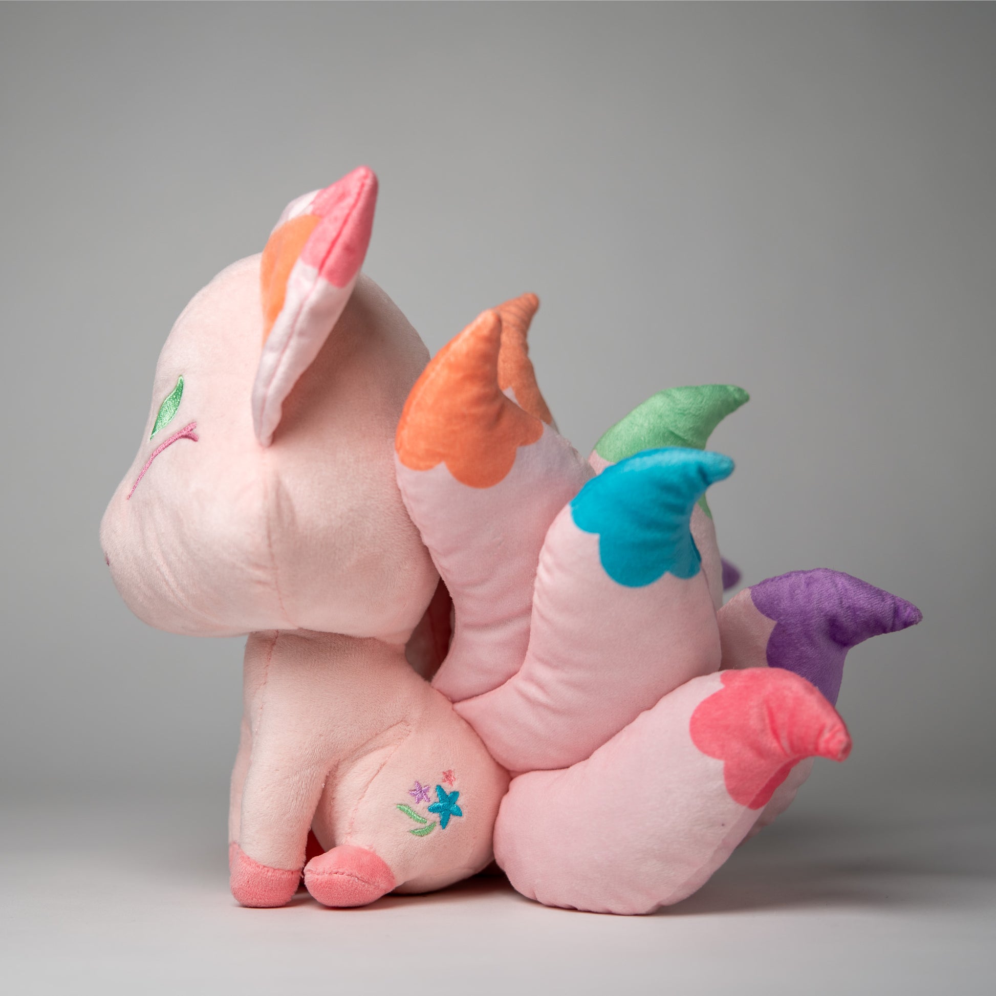 Three-quarter view of Flora, a pink, white, turquoise kitsune plush.