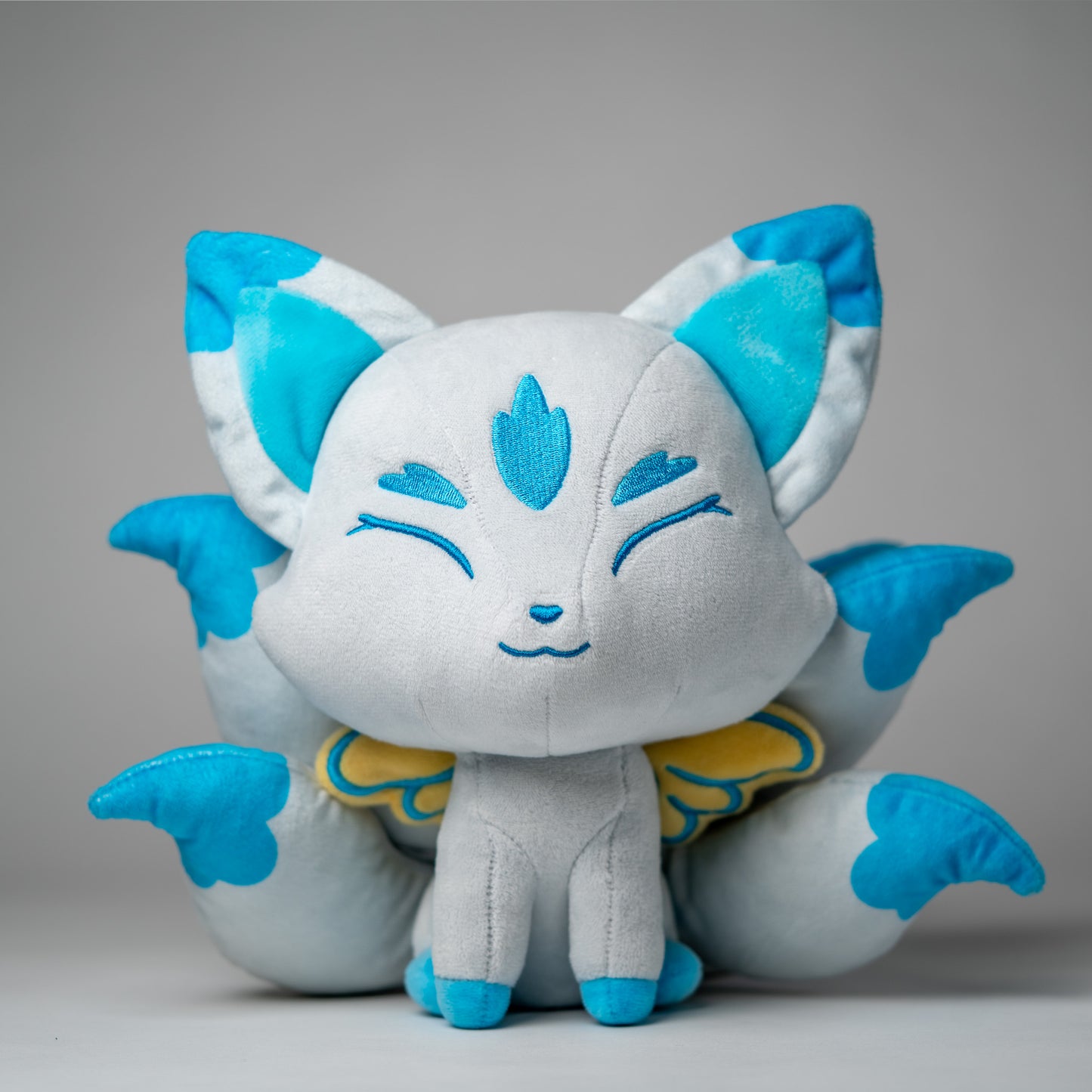 Front view of Icarus, a white, blue, turquoise kitsune plush.