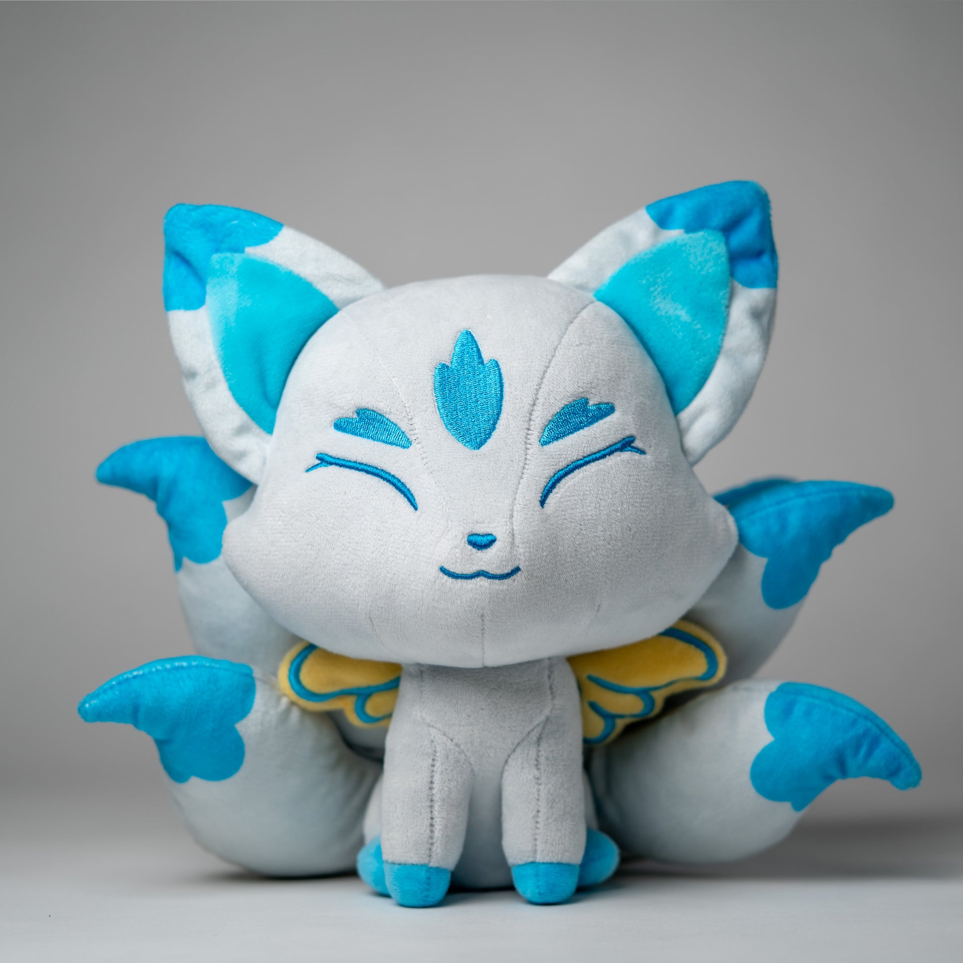Front view of Icarus, a white, blue, turquoise kitsune plush.
