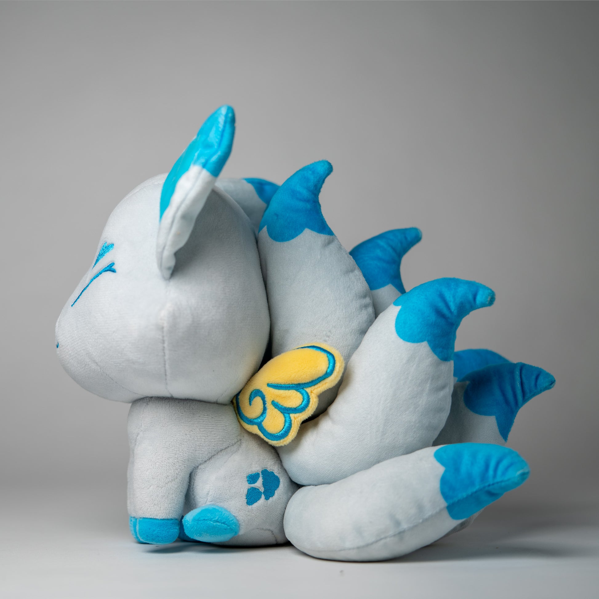 Three-quarter view of Icarus, a white, blue, turquoise kitsune plush.