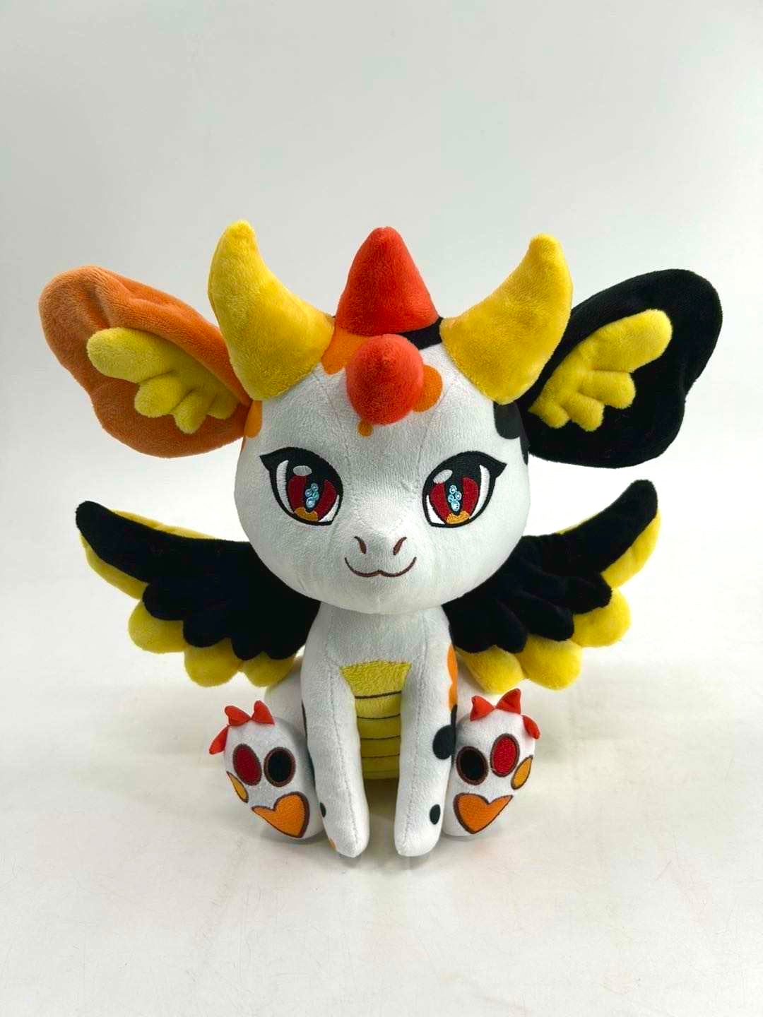 Front view of Kai, a white, black, orange dragon plush.