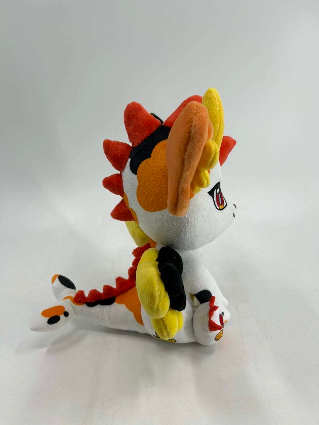 Side view of Kai, a white, black, orange dragon plush.