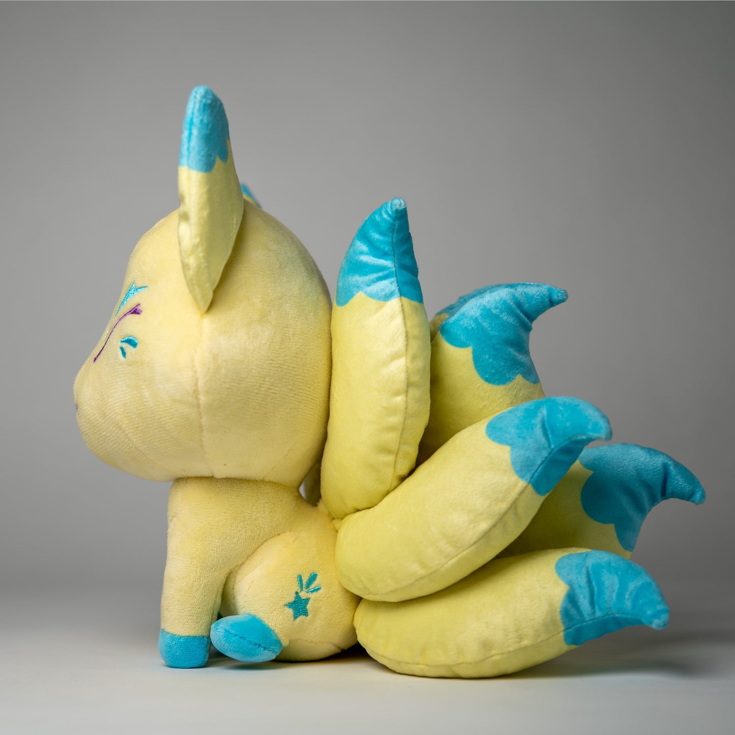 Three-quarter view of Nova, a yellow, turquoise, green kitsune plush.
