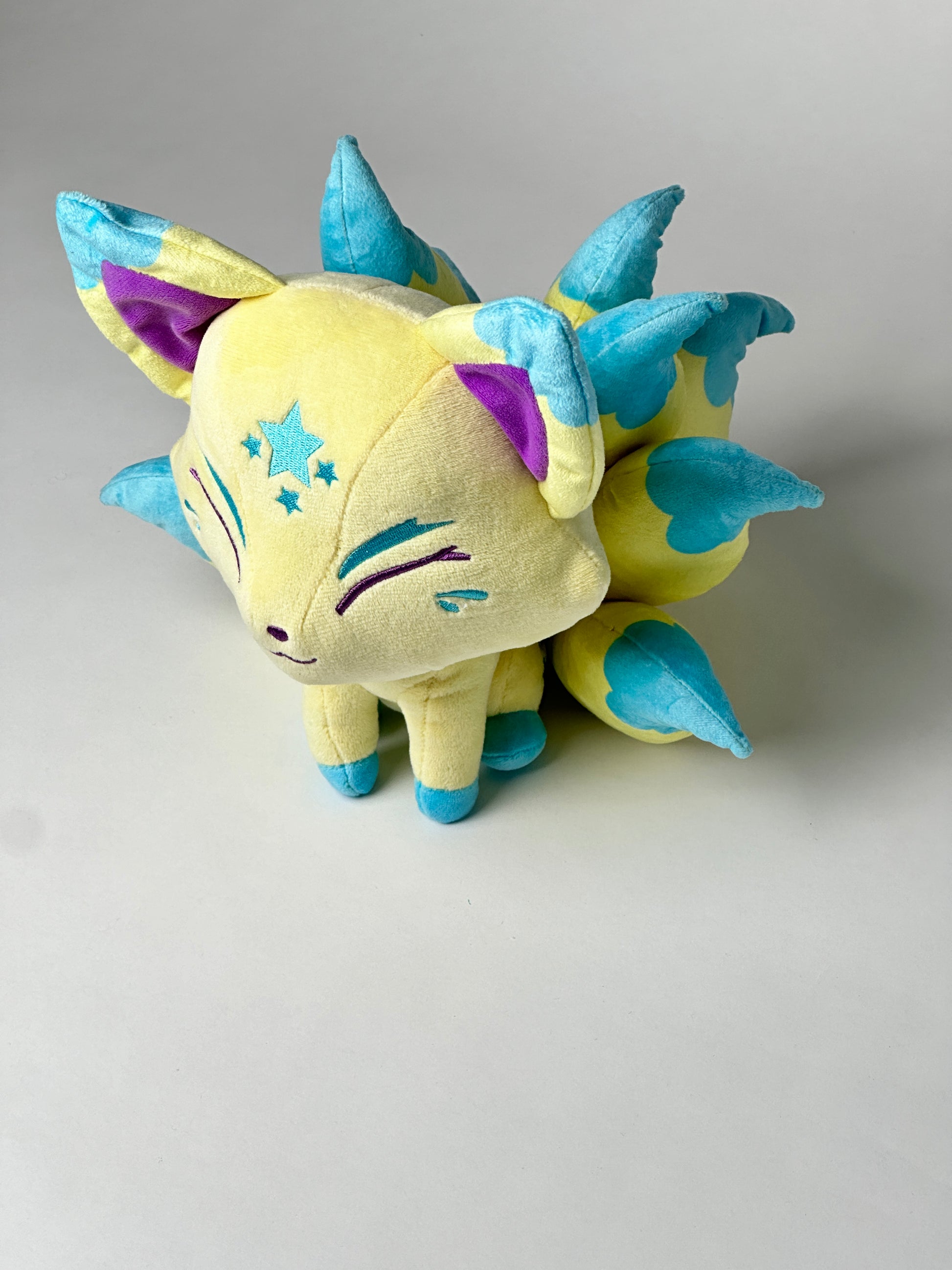 Top view of Nova, a yellow, turquoise, green kitsune plush.