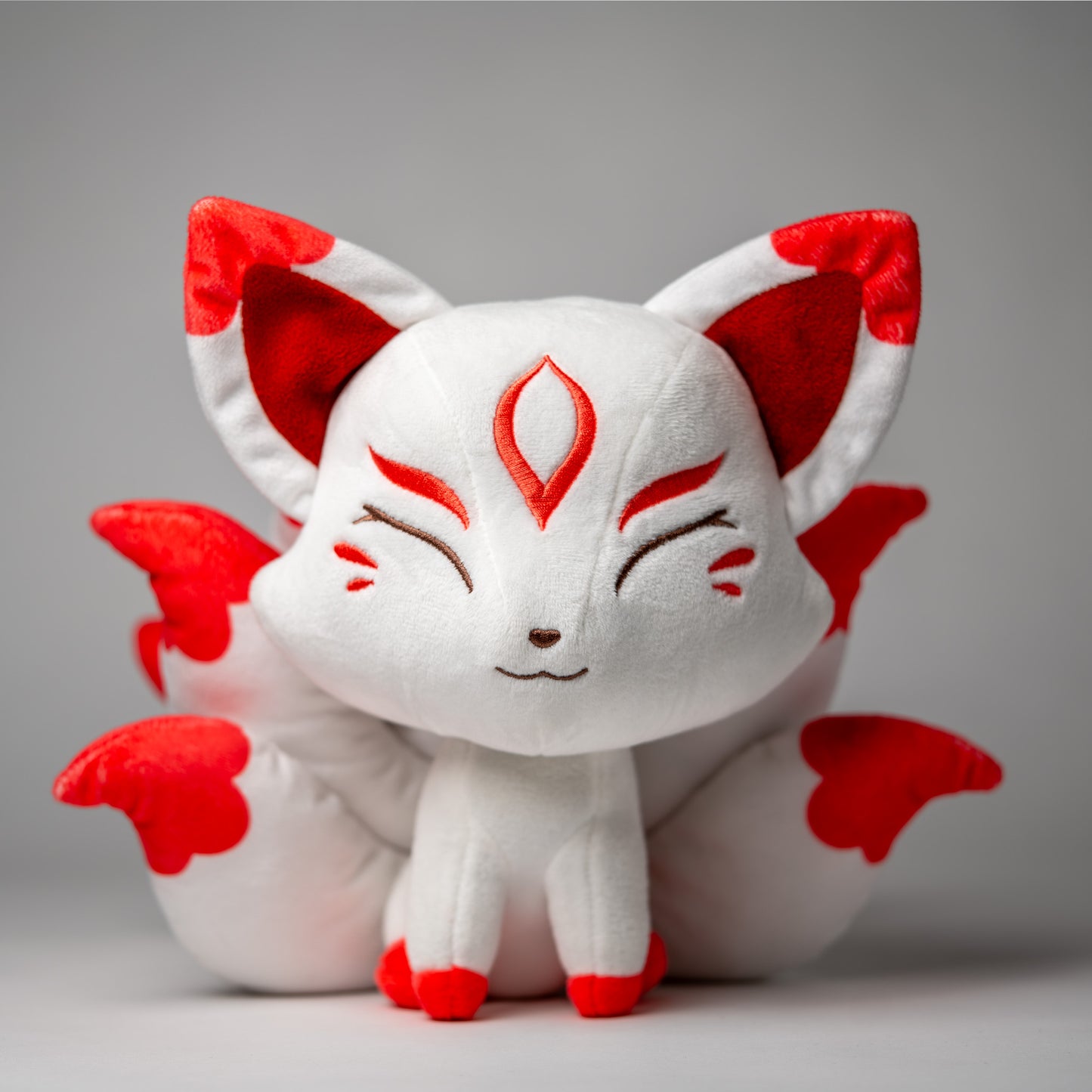 Front view of Okamisu, a white, red, gray kitsune plush.