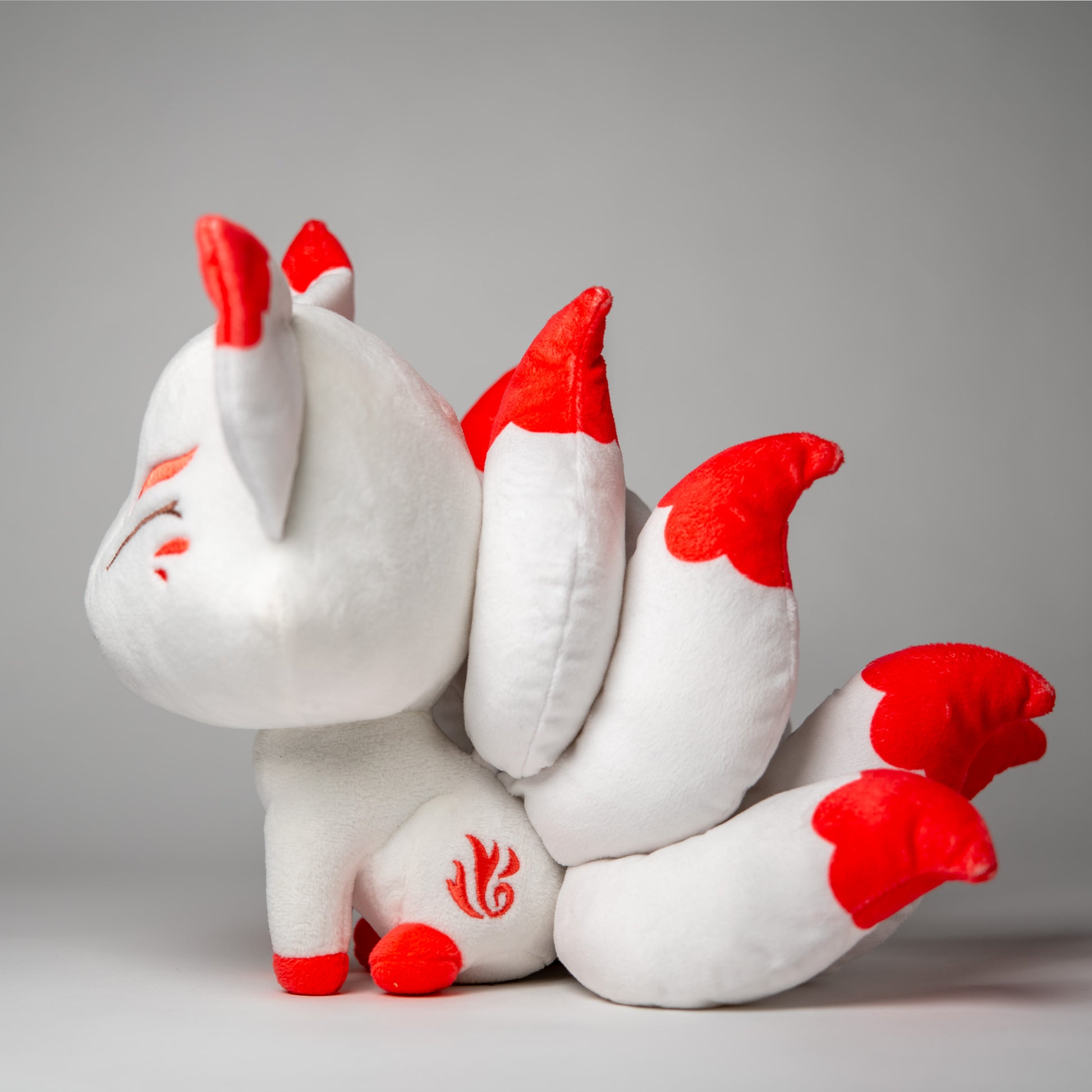Three-quarter view of Okamisu, a white, red, gray kitsune plush.