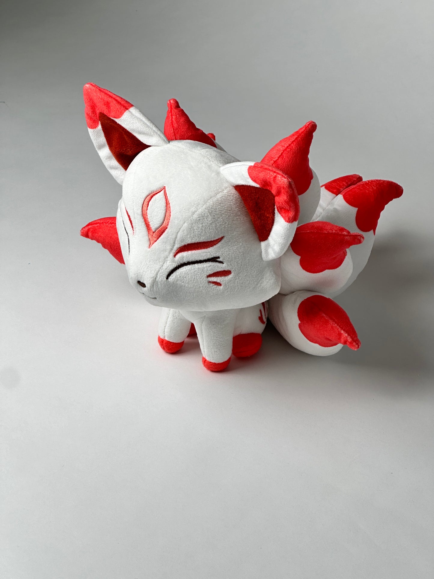 Top view of Okamisu, a white, red, gray kitsune plush.