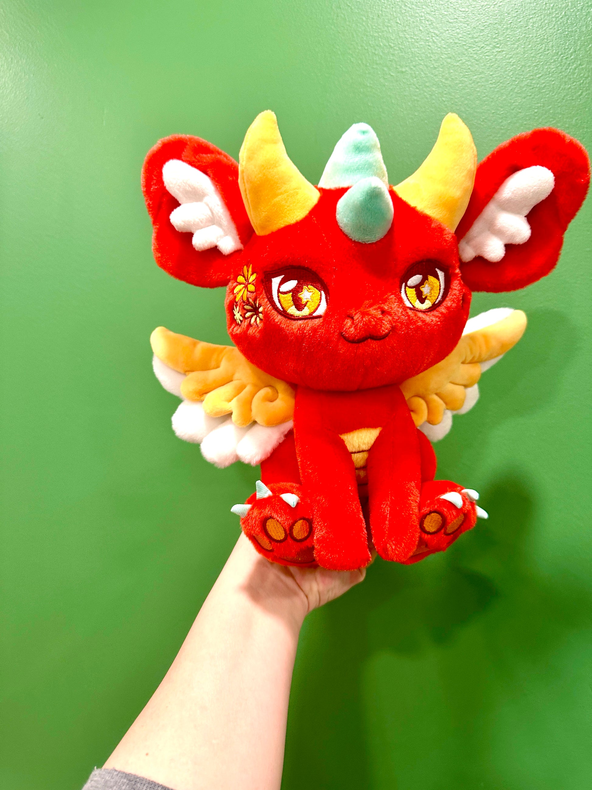 Handheld scale view of Ryu, a red, orange, turquoise dragon plush.