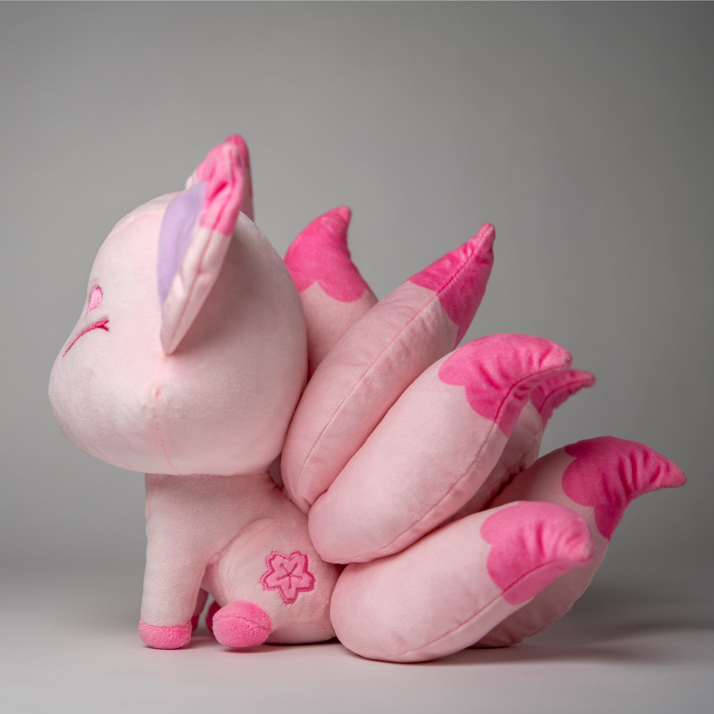 Three-quarter view of Sakura, a pink, rose, lavender kitsune plush.