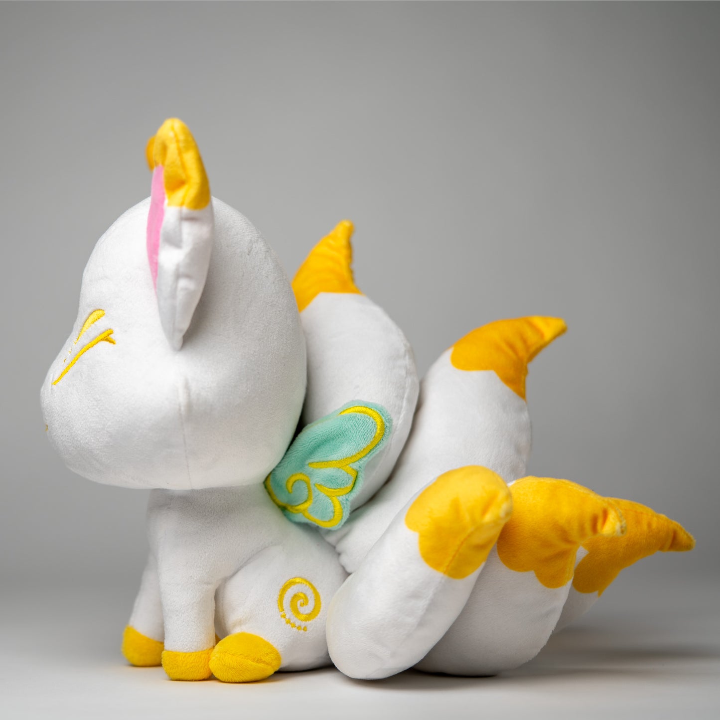 Three-quarter view of Serenity, a white, yellow, mint kitsune plush.