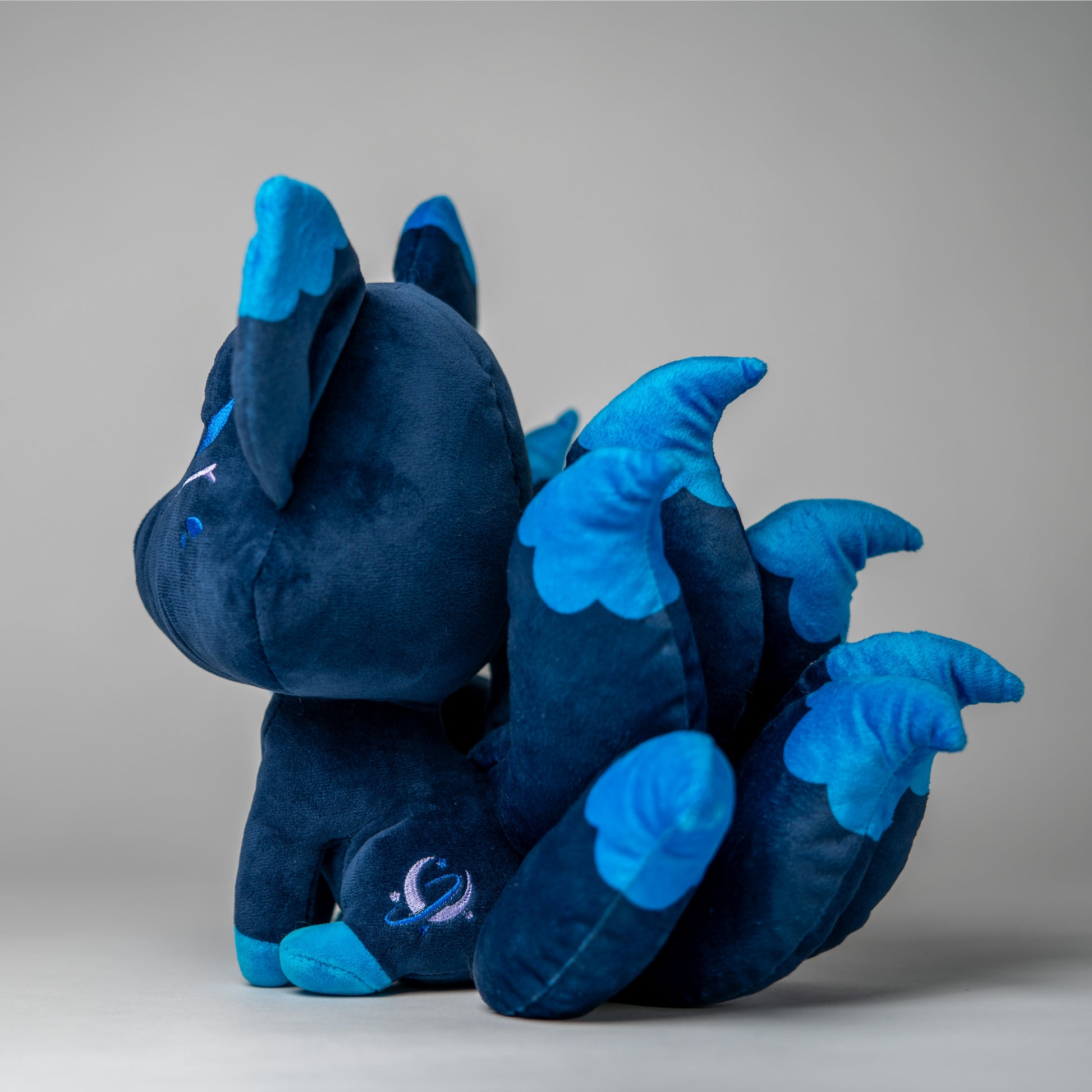 Three-quarter view of Zenith, a navy, blue, turquoise kitsune plush.